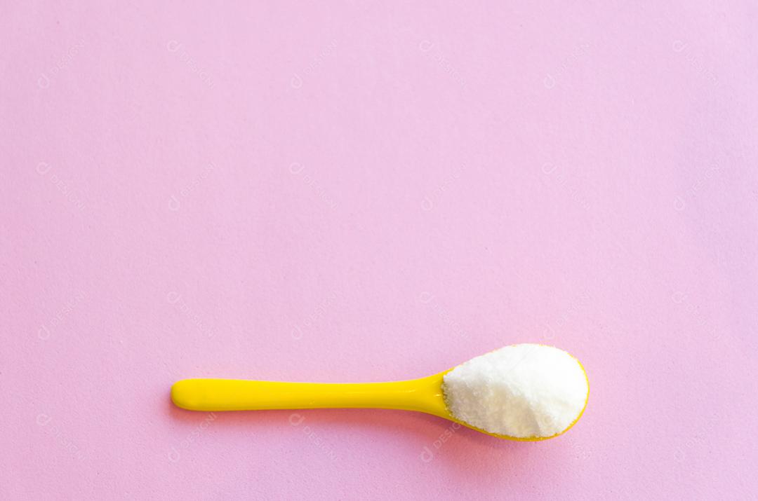 Colher com açúcar close-up em um fundo rosa