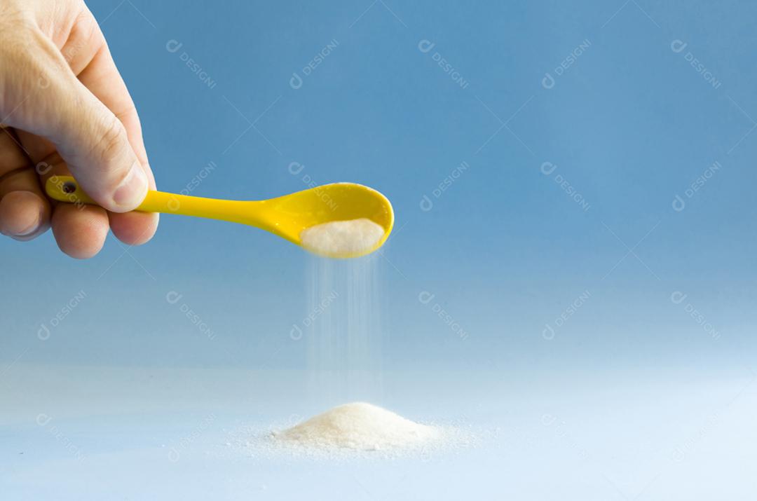 Colher amarela virando açúcar no fundo azul