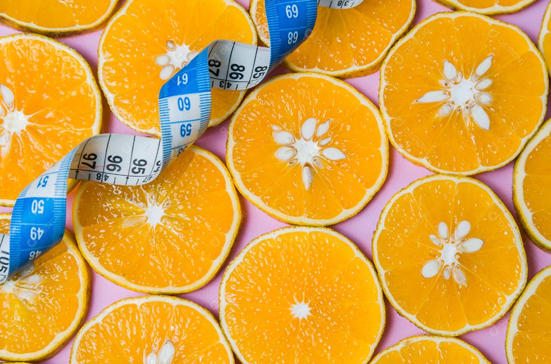 Fundo para o conceito de alimentação saudável fatias de laranja em fundo rosa com fita métrica