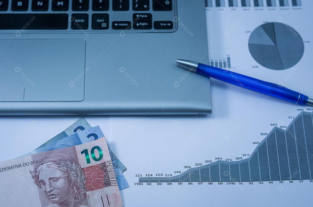 Computador portátil, caneta, gráficos, cartão de crédito e dinheiro brasileiro