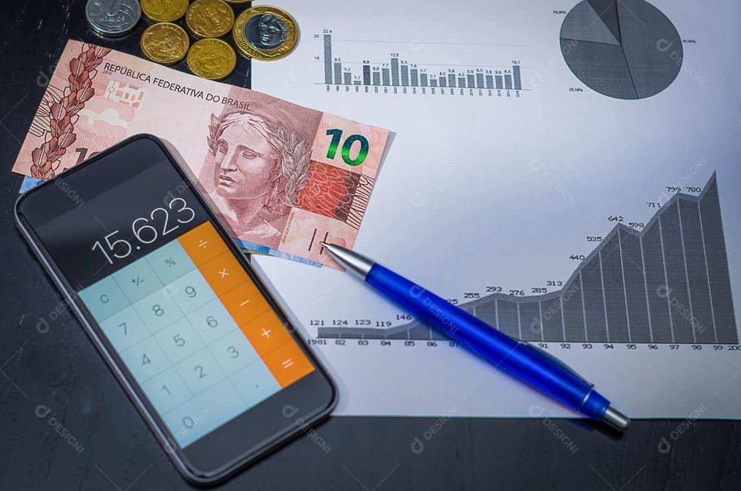 Smartphone, caneta, gráficos, calculadora, cartão de crédito e dinheiro brasileiro (real), conceito de finanças