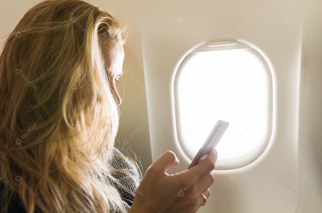 Jovem loira usando smartphone no avião