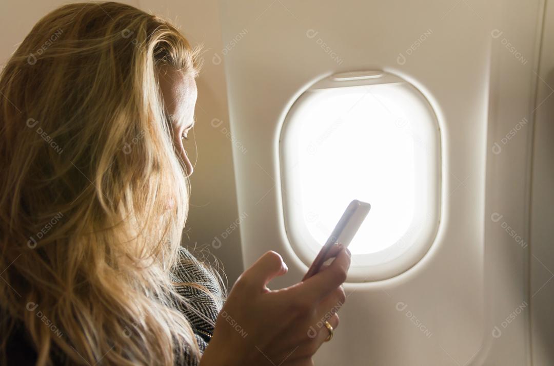 Jovem loira usando smartphone no avião