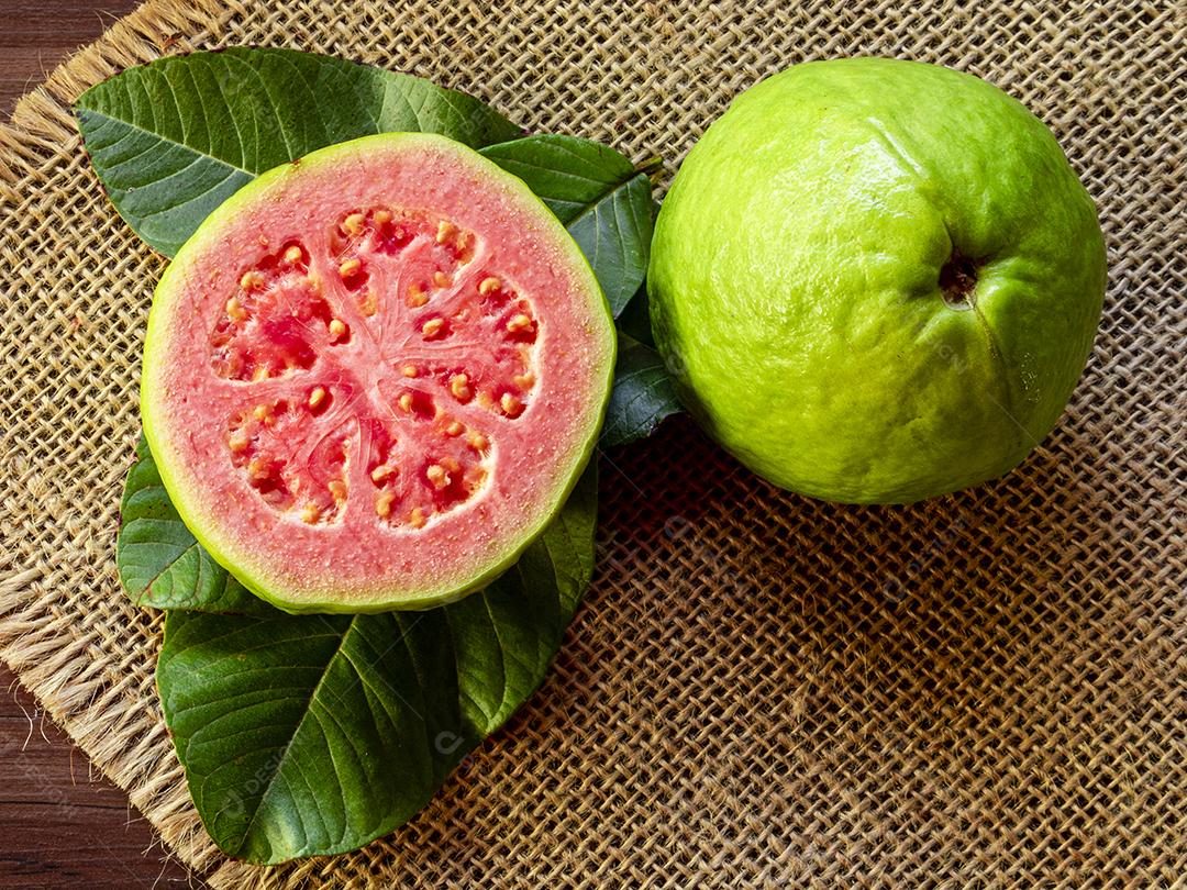 Goiabas vermelhas frescas com folhas verdes no fundo de demolição de madeira