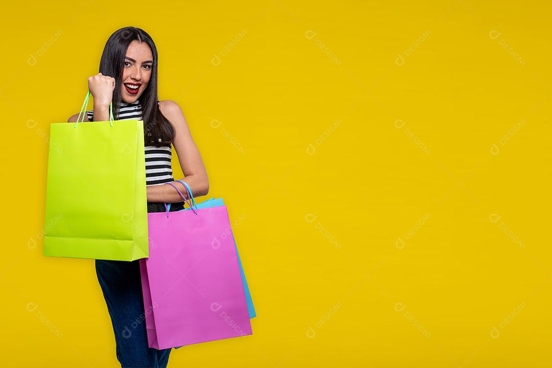 Mulher sorridente segurando sacolas de compras, isolada em fundo amarelo