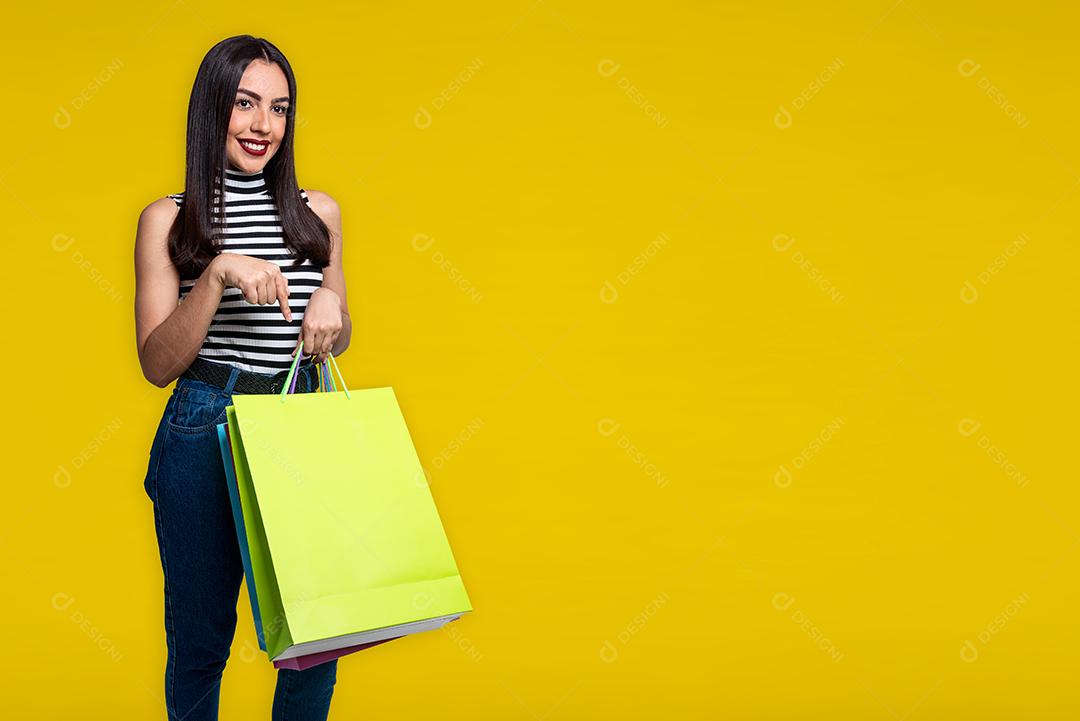 Mulher sorridente segurando sacolas de compras, isolada em fundo amarelo