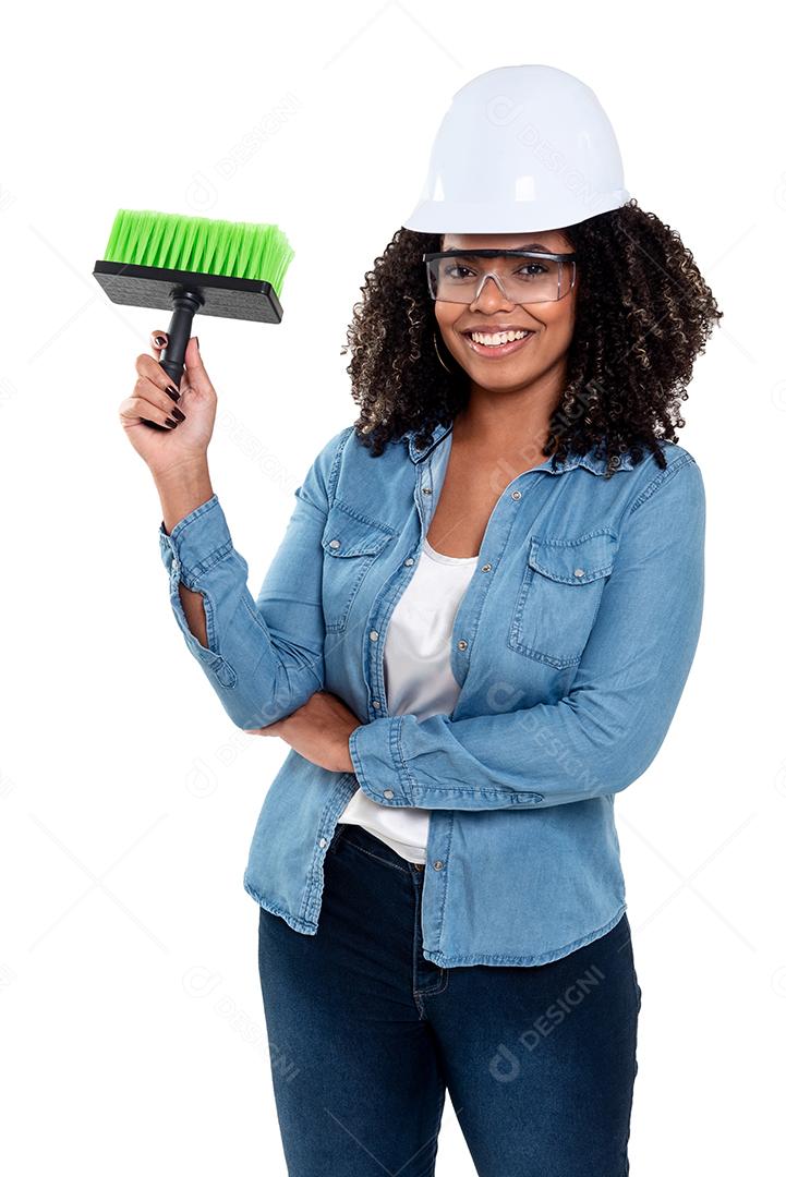 Mulher negra brasileira alegre e sorridente isolada de fundo branco, trabalhando com um pincel usando óculos e capacete na cabeça.