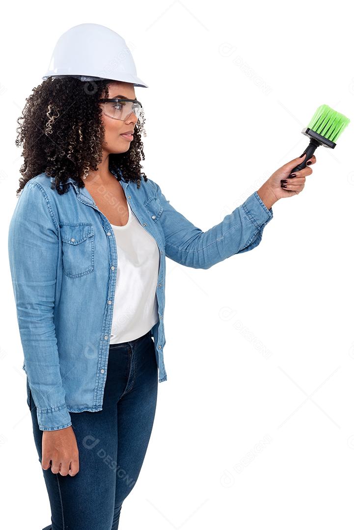 Mulher negra brasileira alegre e sorridente isolada de fundo branco, trabalhando com um pincel usando óculos e capacete na cabeça.