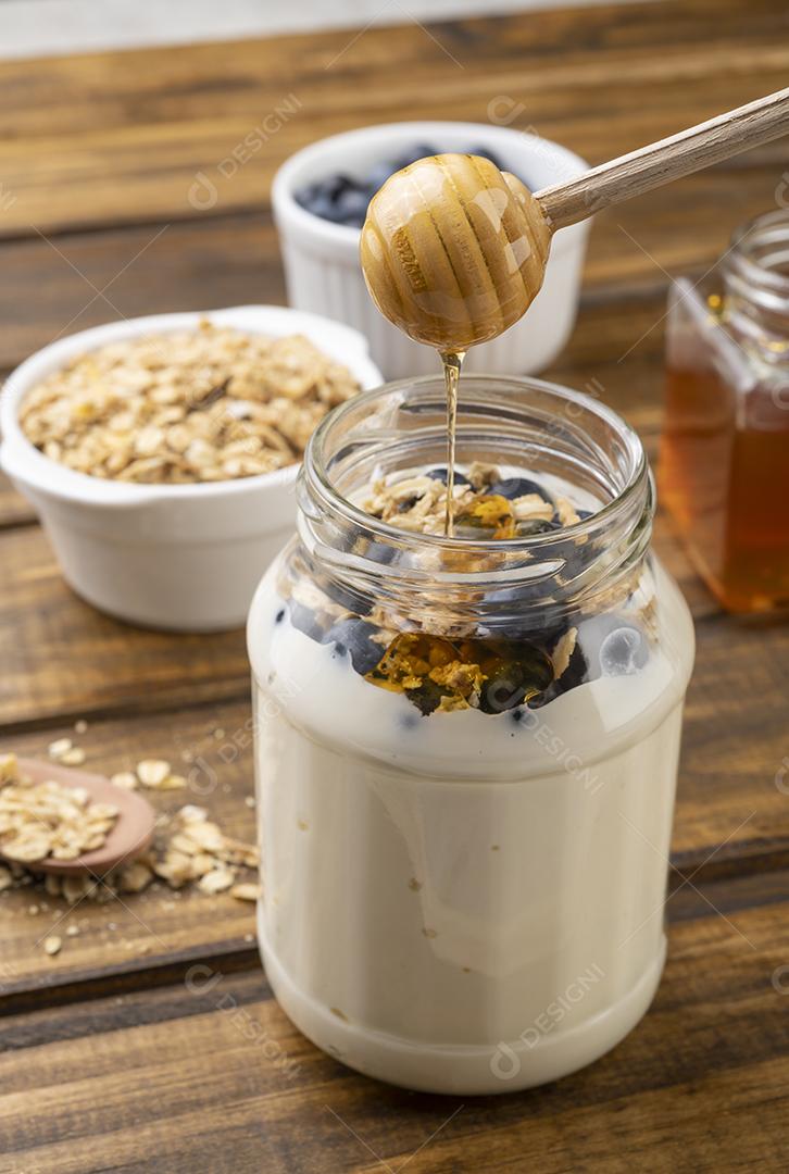 Iogurte, granola, bluberry e mel sobre mesa de madeira. Utensílio de madeira