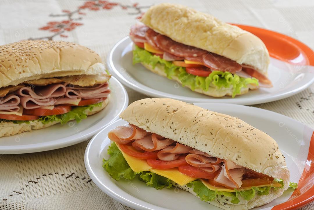 Sanduíches de presunto, salame, queijo, alface e tomate na mesa.