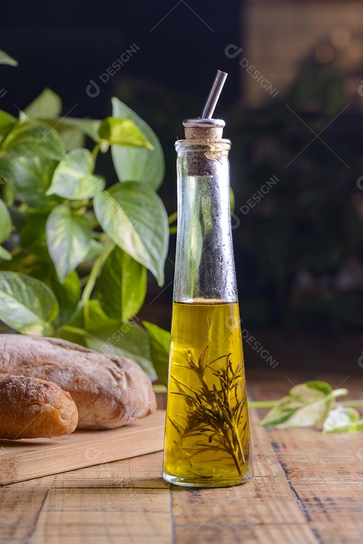 Azeite de oliva com alecrim em uma garrafa de vidro na mesa de madeira com pães.