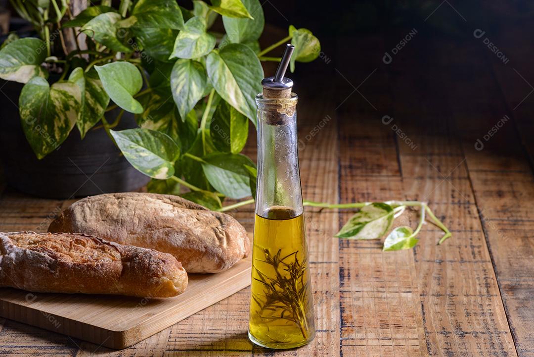 Azeite de oliva com alecrim em uma garrafa de vidro na mesa de madeira com pães.