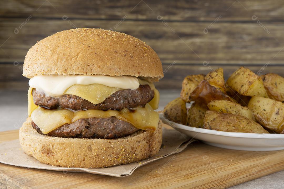 Cheeseburger duplo sobre tábua de madeira com batatas assadas
