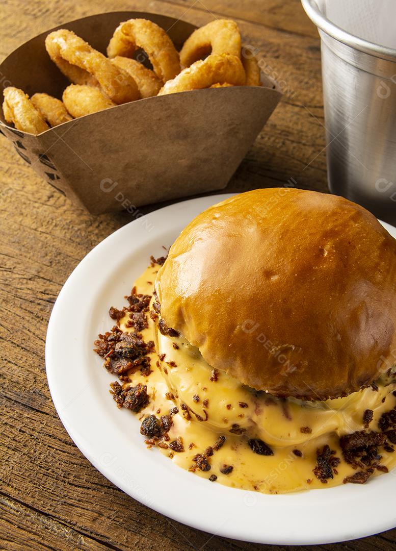 Queijo derretido e hambúrguer de bacon com anéis de cebola sobre madeira