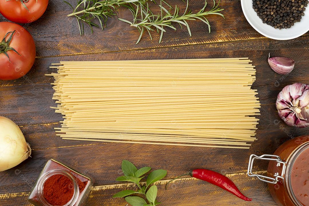 Espaguete, tomate, alho, pimentas e ervas sobre mesa de madeira