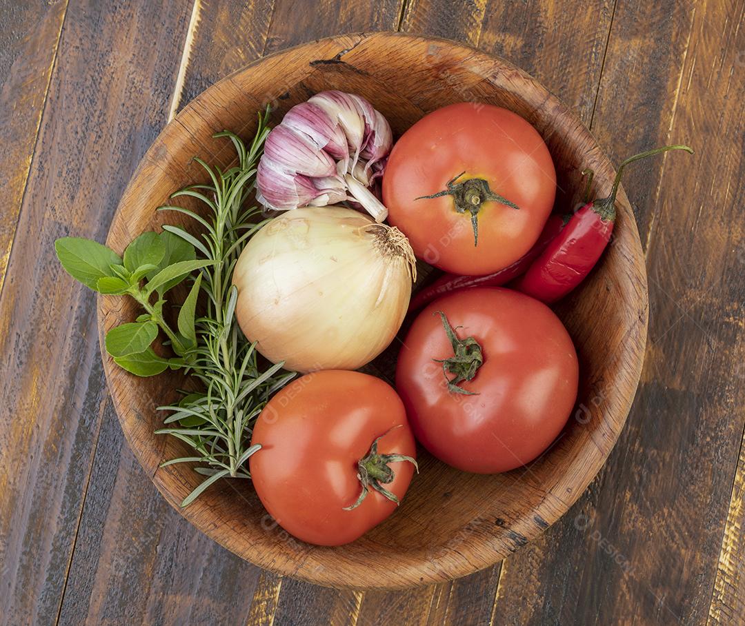Tomates, alho, pimentas e ervas em uma tigela sobre a mesa de madeira.