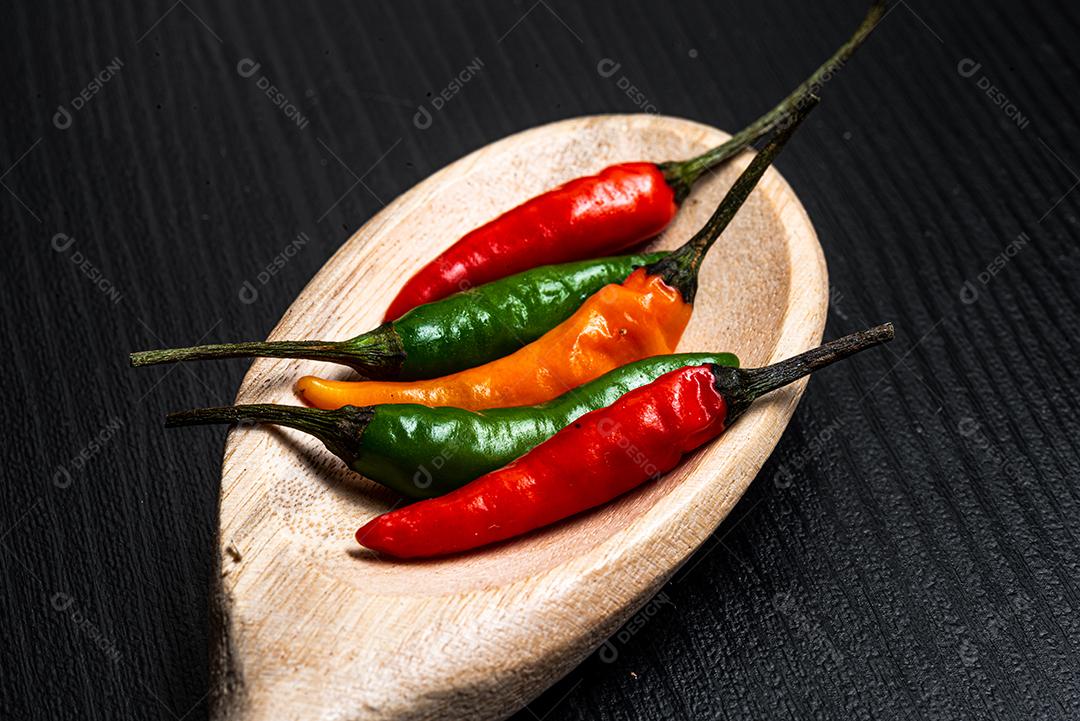 Vários pimentões quentes dentro de uma colher de madeira em um fundo de madeira rústica preta