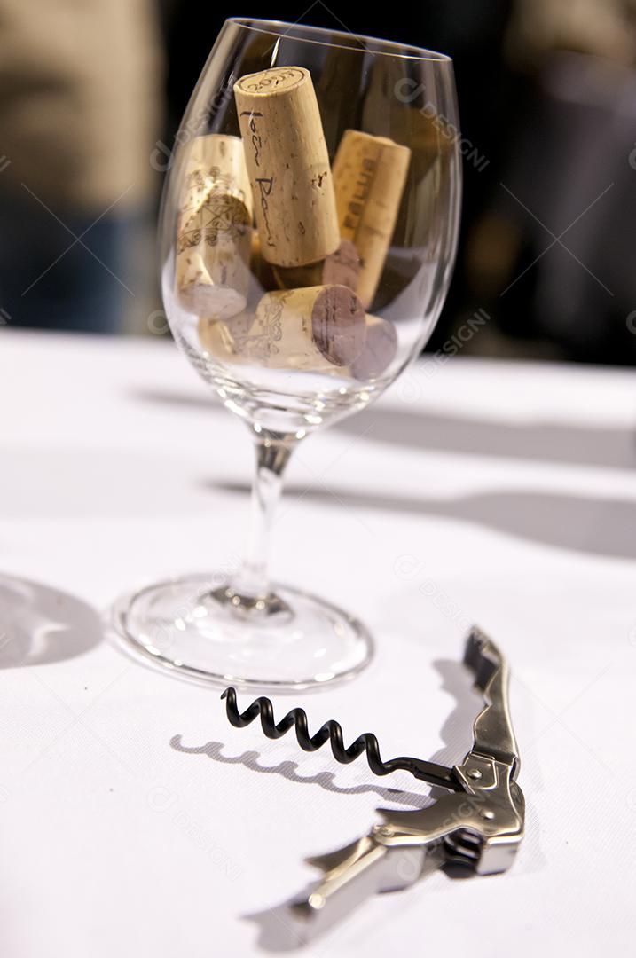 Taça de cristal com rolha e sacarolha sobre mesa branca