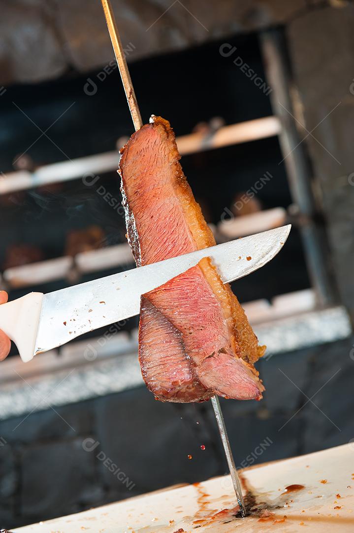 Churrasco no espeto. Churrasqueira, carne assada sendo cortada