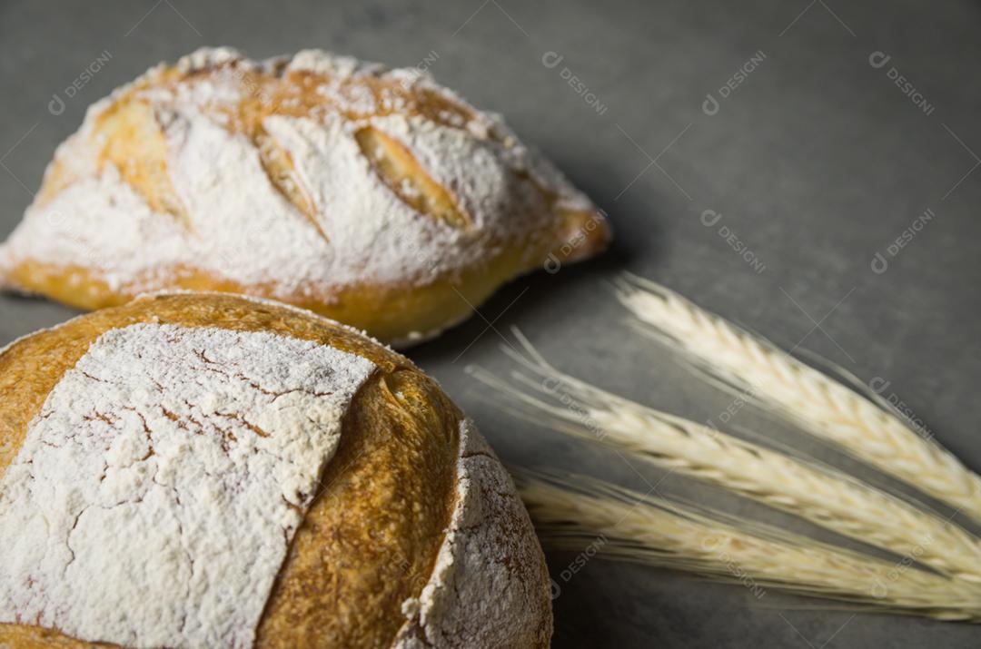 Belo pão de fermento em fundo cinza com flor de trigo seca.