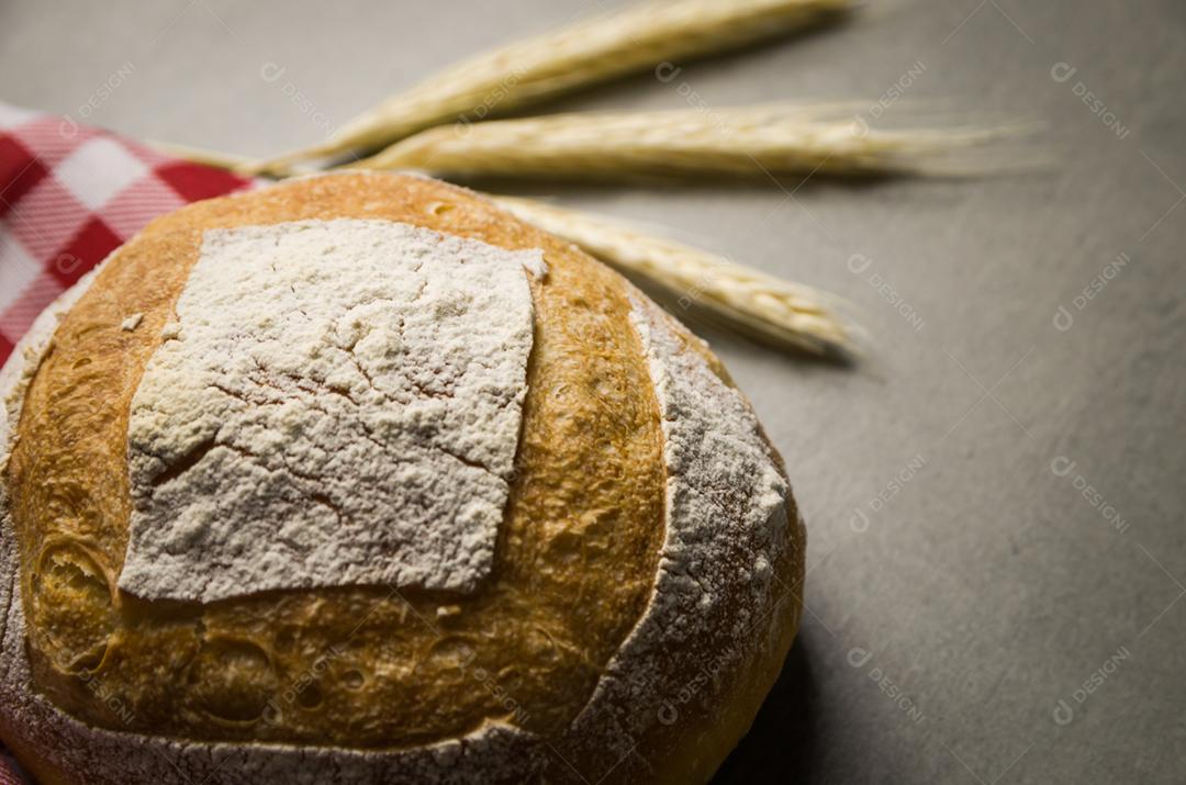 Belo pão de fermento em fundo cinza com flor de trigo seca.