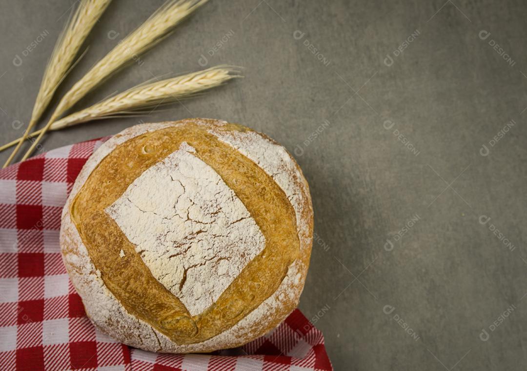 Belo pão de fermento em fundo cinza com flor de trigo seca.