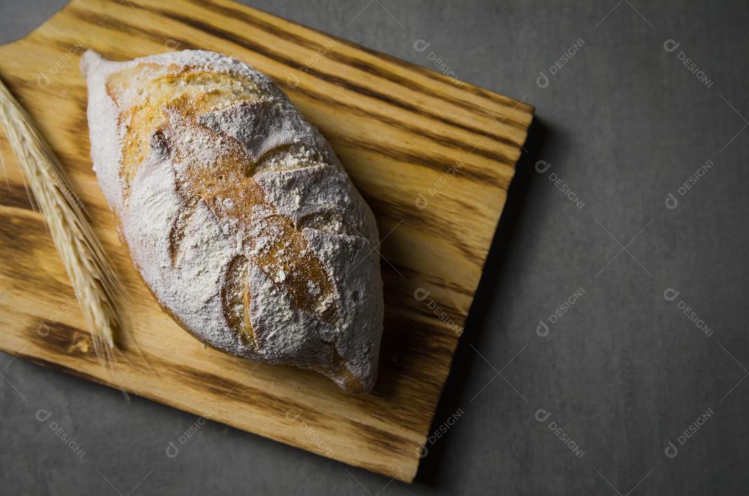 Belo pão de fermento em fundo cinza com flor de trigo seca.