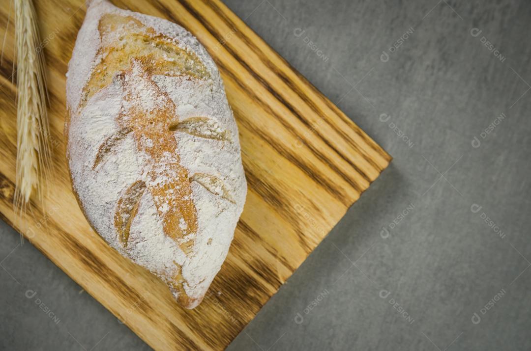 Belo pão de fermento em fundo cinza com flor de trigo seca.