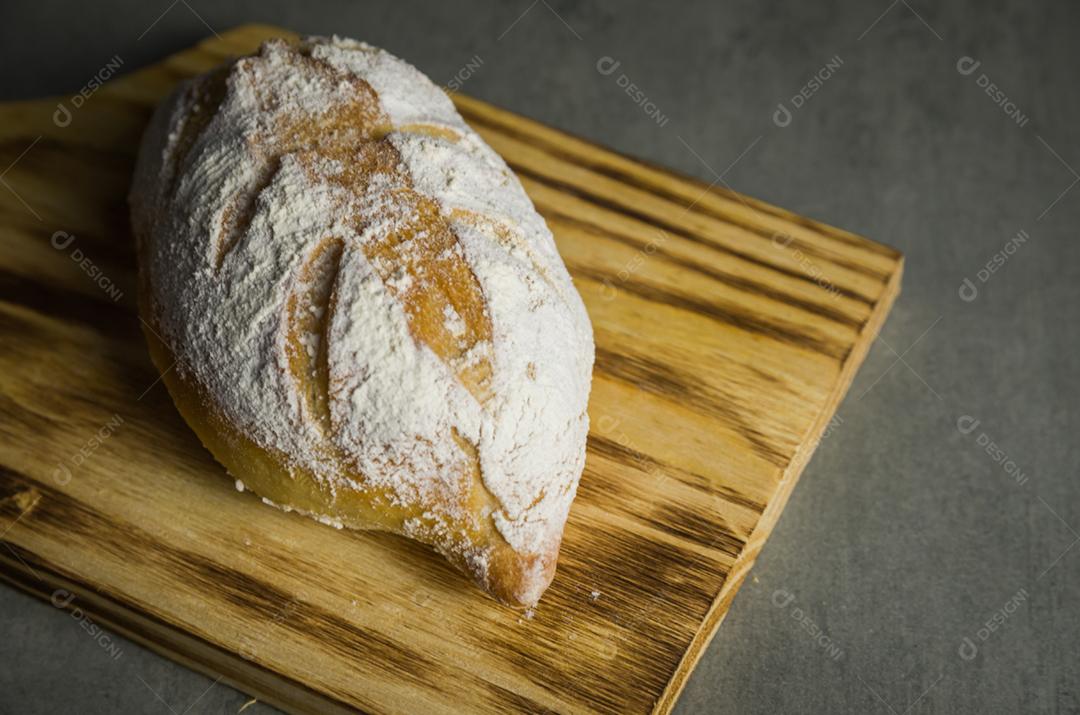 Belo pão de fermento em fundo cinza com flor de trigo seca.