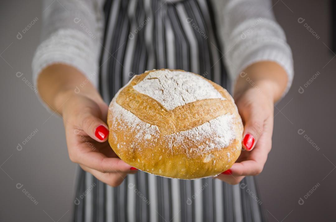 Pão de fermento bonito sendo realizado pelas mãos da mulher e fundo desfocado.