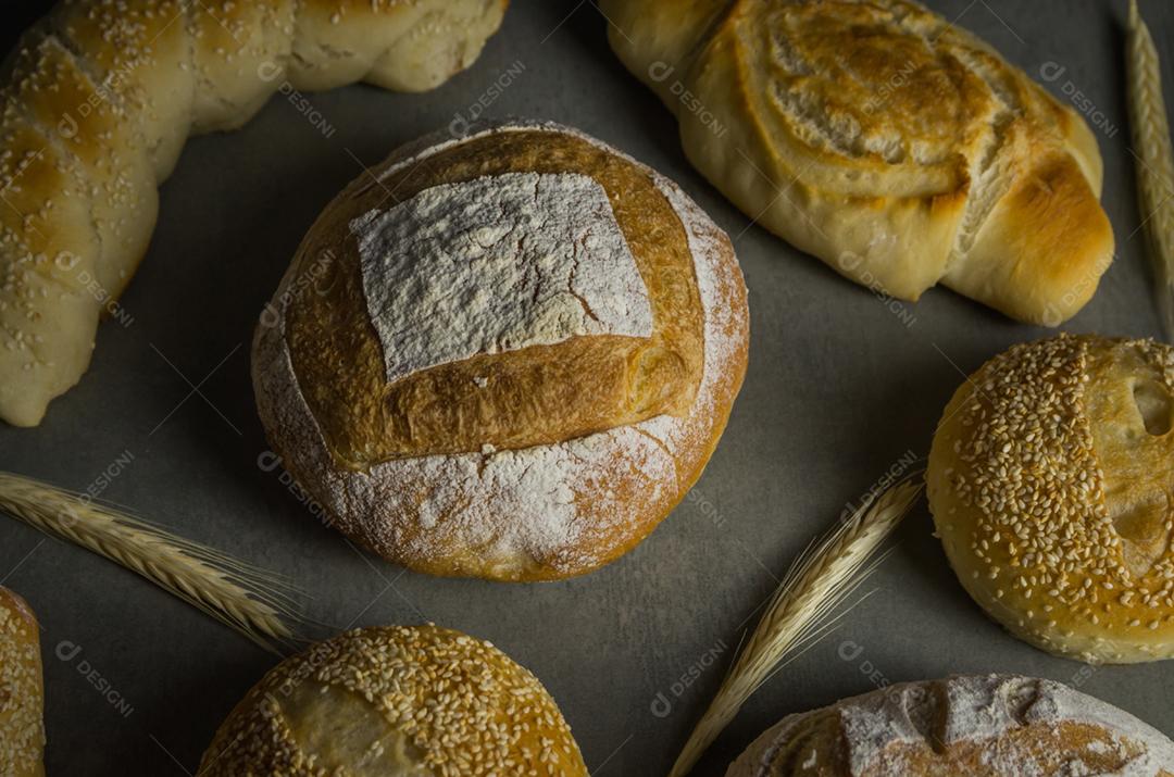 Belo pão de fermento em fundo cinza com flor de trigo seca.