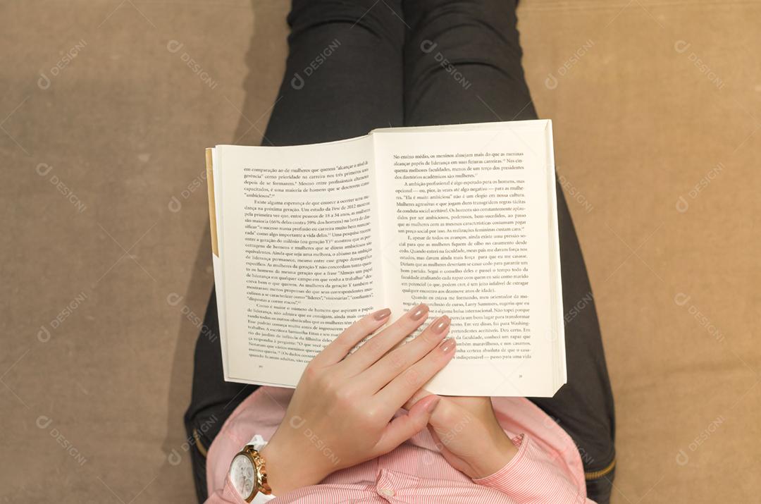 Mulher lendo livro no sofá, relaxando. Ambiente decorado.