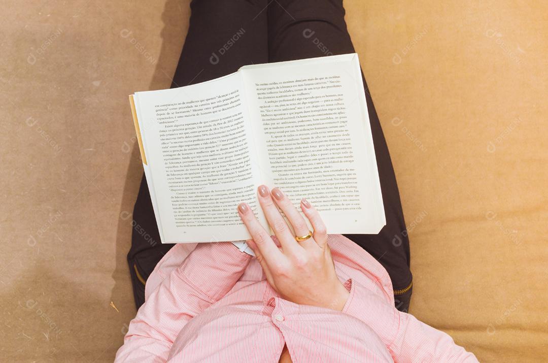 Mulher lendo livro no sofá, relaxando. Ambiente decorado.