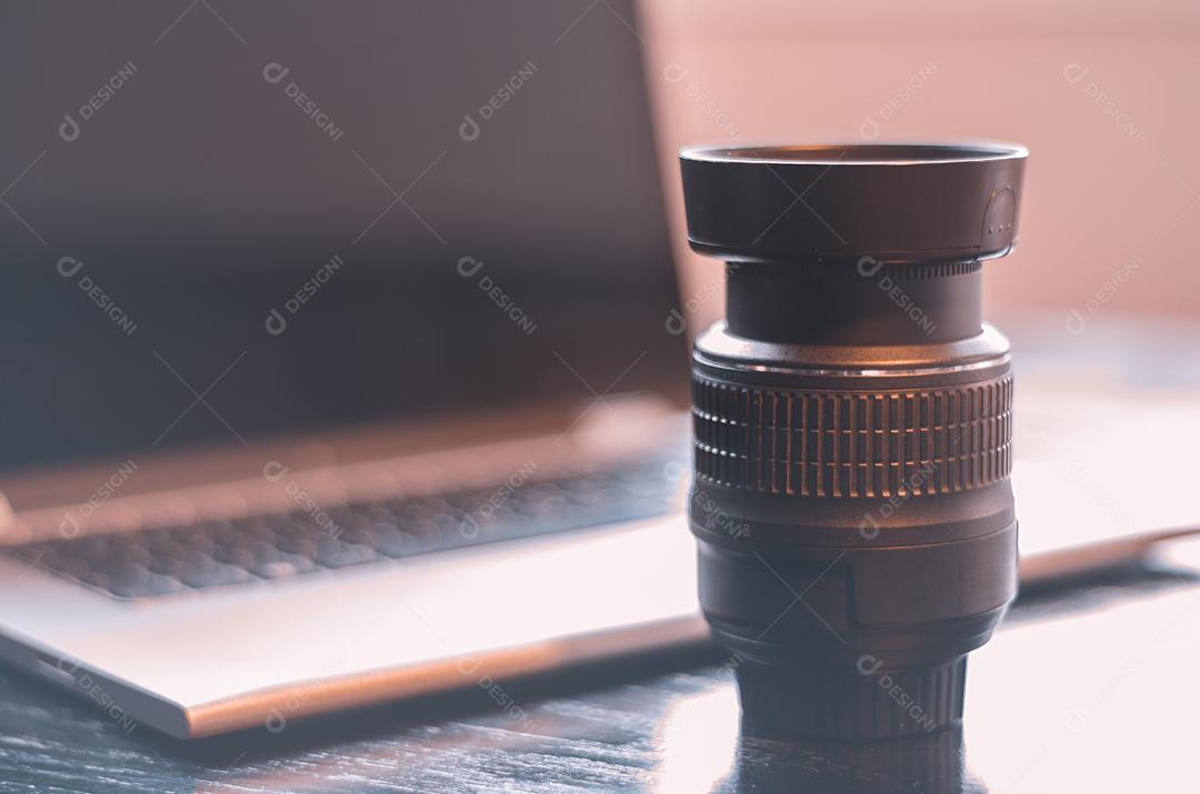 Mesa com equipamento fotográfico, computador e lente.