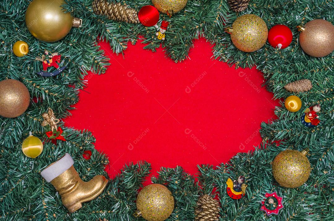 Fundo com tema natalino, folhas de pinheiro nas bordas de papel vermelho e objetos decorativos.