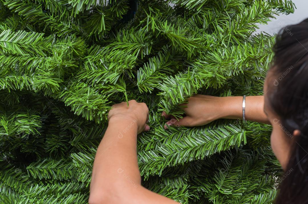 Mãos de mulher arrumando e decorando a árvore de natal