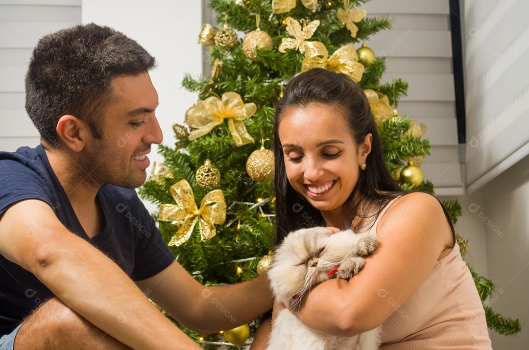 Casal sentado em frente ao pinheiro de Natal com animal de estimação, gato.