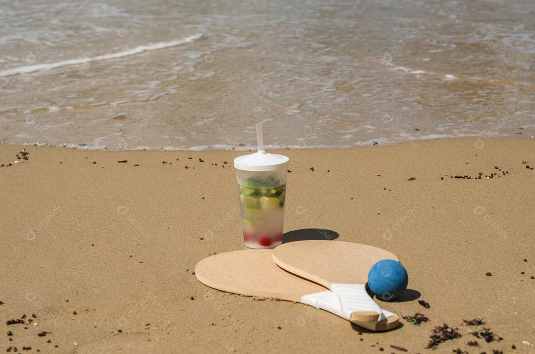 Raquetes de tênis de praia na areia, bebida caipirinha