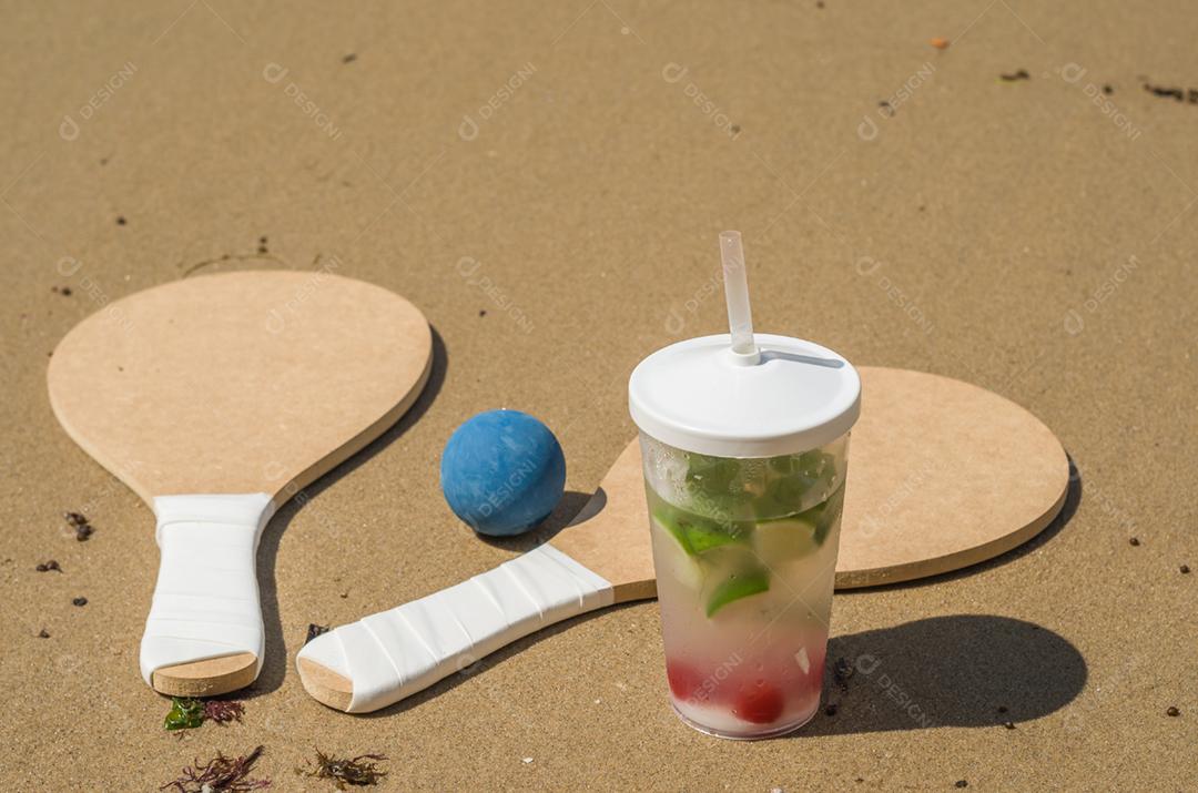 Raquetes de tênis de praia na areia, bebida caipirinha