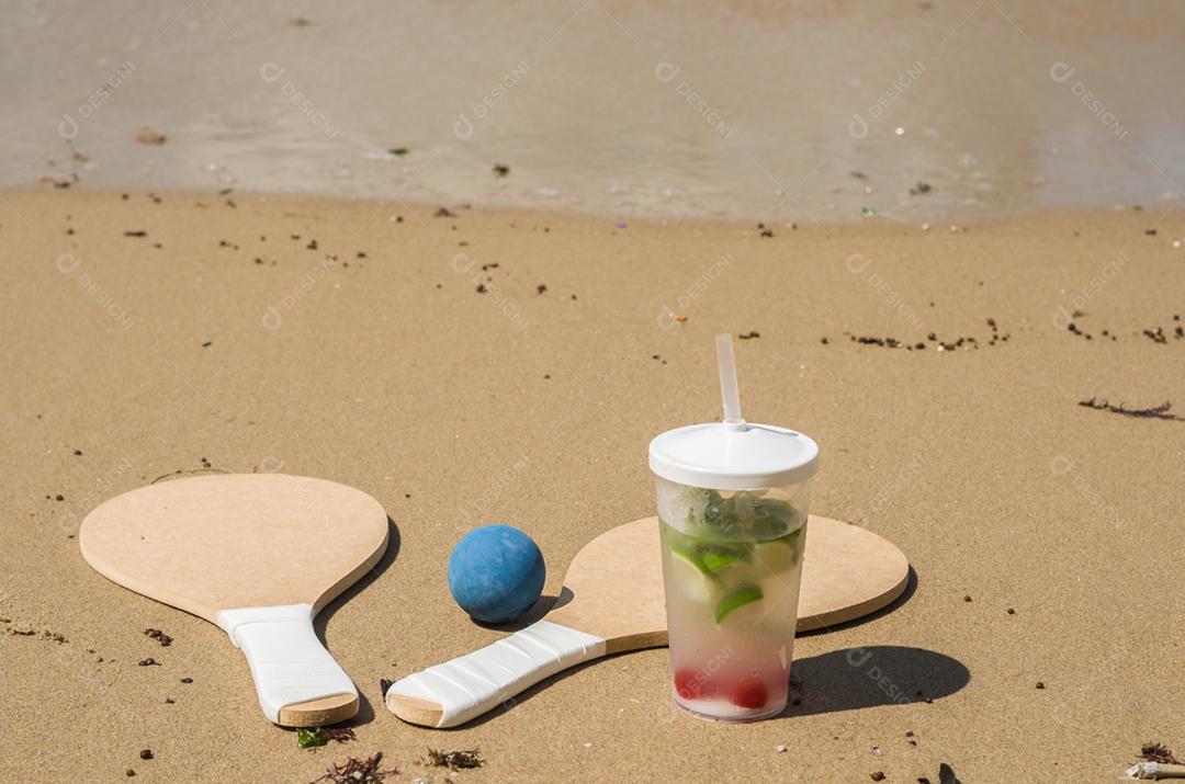 Raquetes de tênis de praia na areia, bebida caipirinha