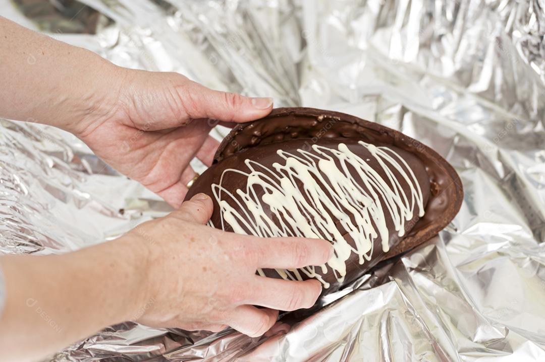 Mãos de mulher quebrando um ovo de Páscoa. Embalagem prata de fundo.