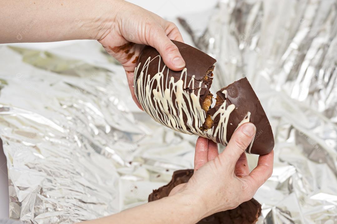 Mãos de mulher quebrando um ovo de Páscoa recheado com trufas.