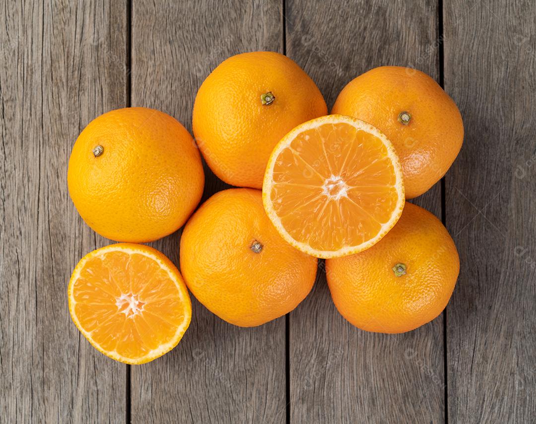 Tangerinas com frutas cortadas sobre mesa de madeira.