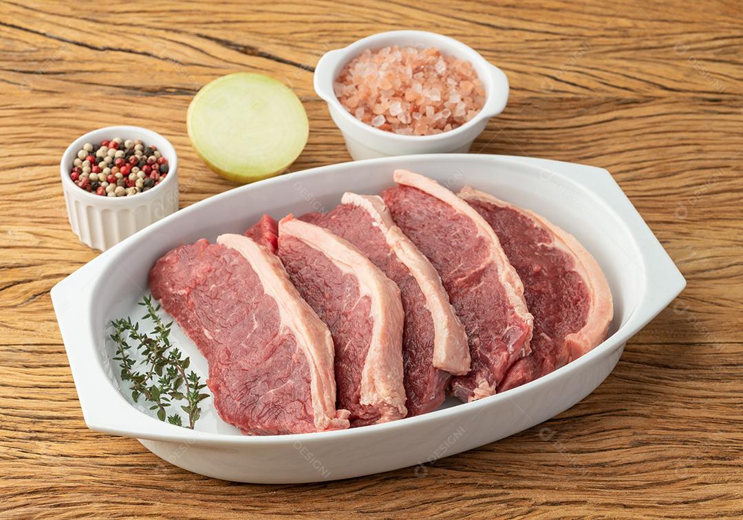 Carne de lombo de tira crua fatiada sobre prato branco com temperos.