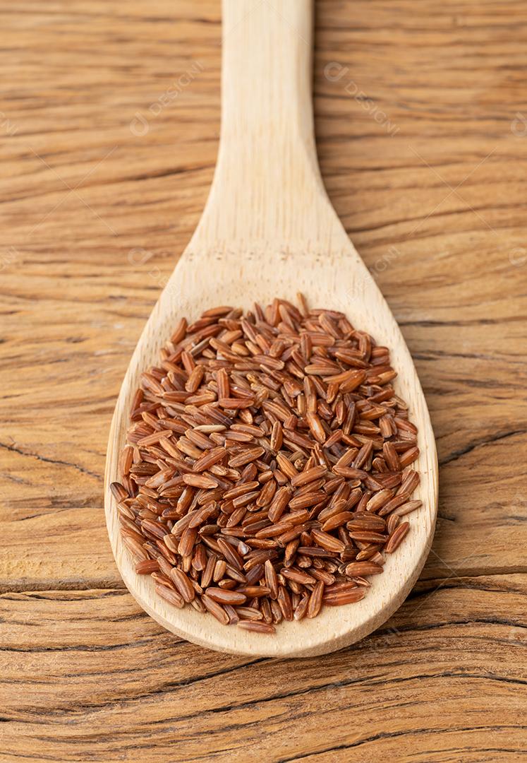Arroz integral vermelho cru em uma colher sobre mesa de madeira