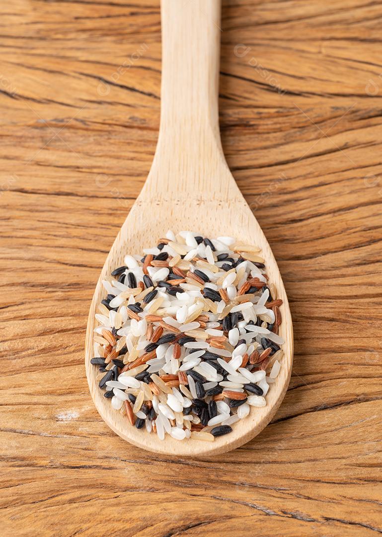 Arroz variado cru em uma colher sobre mesa de madeira