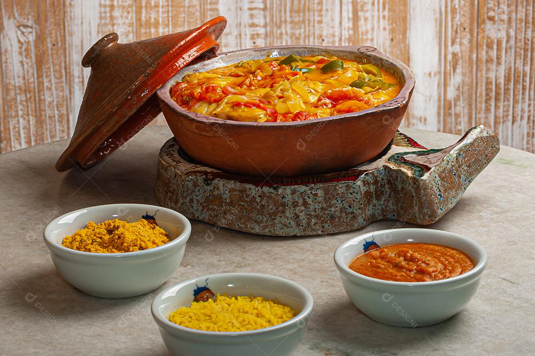 Moqueca de garoutureira servida com arroz de açafrão, farofa e pirão e molho de pimenta. Comida típica brasileira.