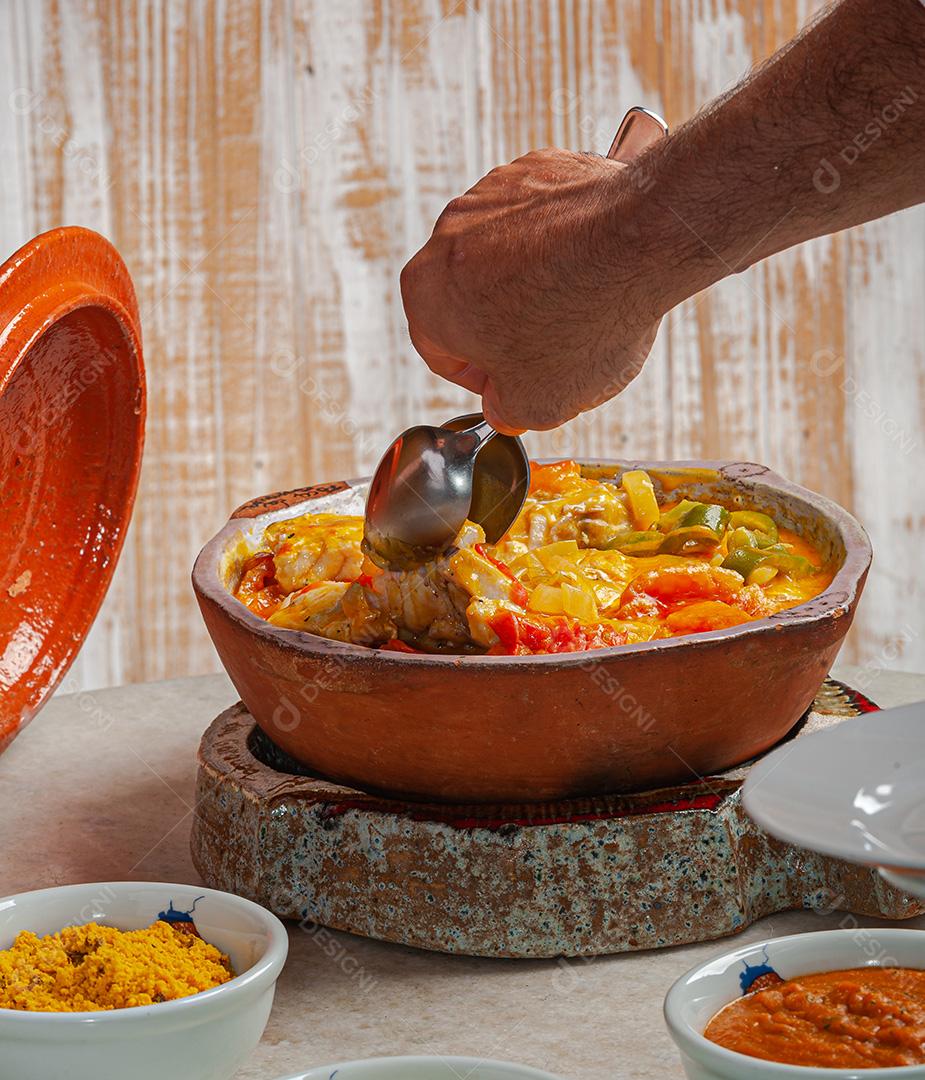 Garçom servindo Moqueca de Garoupa com arroz de açafrão, farofa, pirão e molho de pimenta. Comida típica brasileira