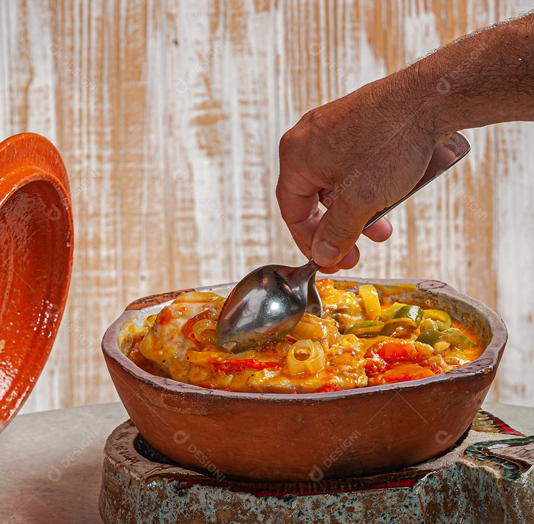 Garçom servindo Moqueca de Garoupa com arroz de açafrão, farofa, pirão e molho de pimenta. Comida típica brasileira