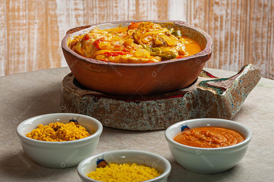 Moqueca de garoutureira servida com arroz de açafrão, farofa e pirão e molho de pimenta. Comida típica brasileira.